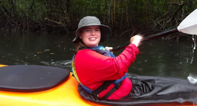 A person wearing a life jacket smiles from inside a yellow kayak